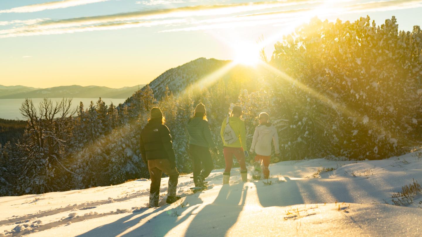 Sunset over snowy mountain, five people in warm clothing admire the view.