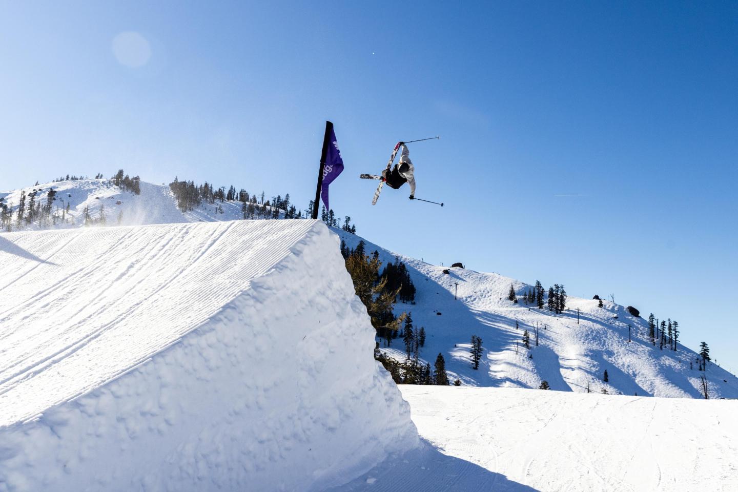 Skier mid-air performing a jump on a snowy mountain under clear blue sky.