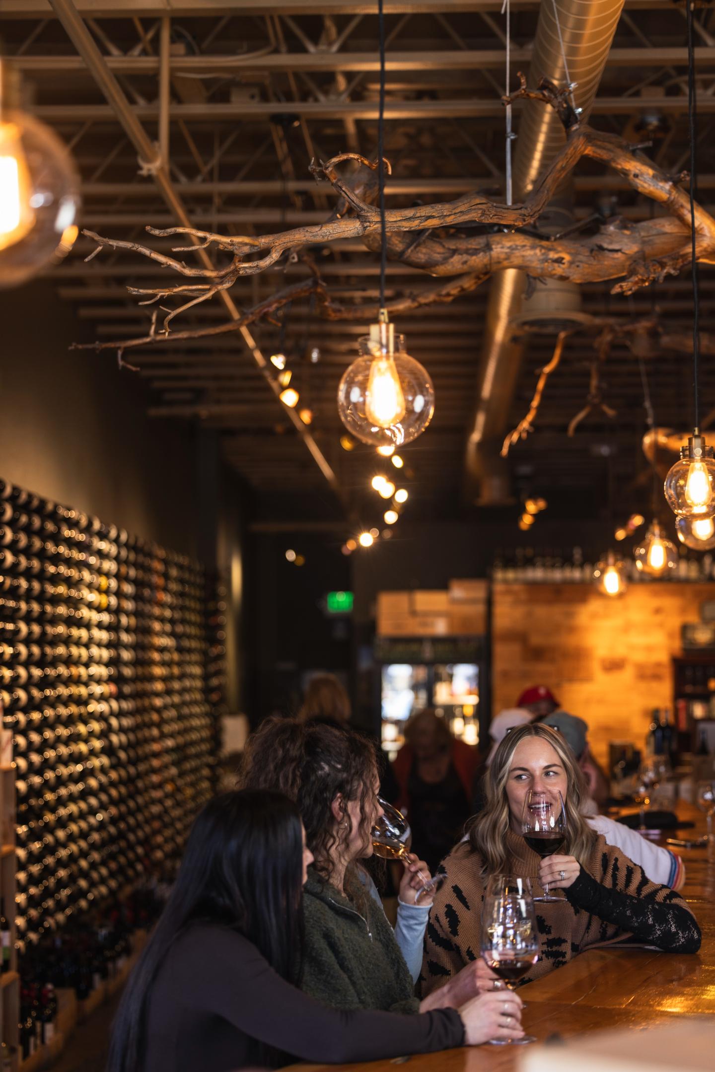 Cozy wine bar with people enjoying drinks under warm, hanging lights.