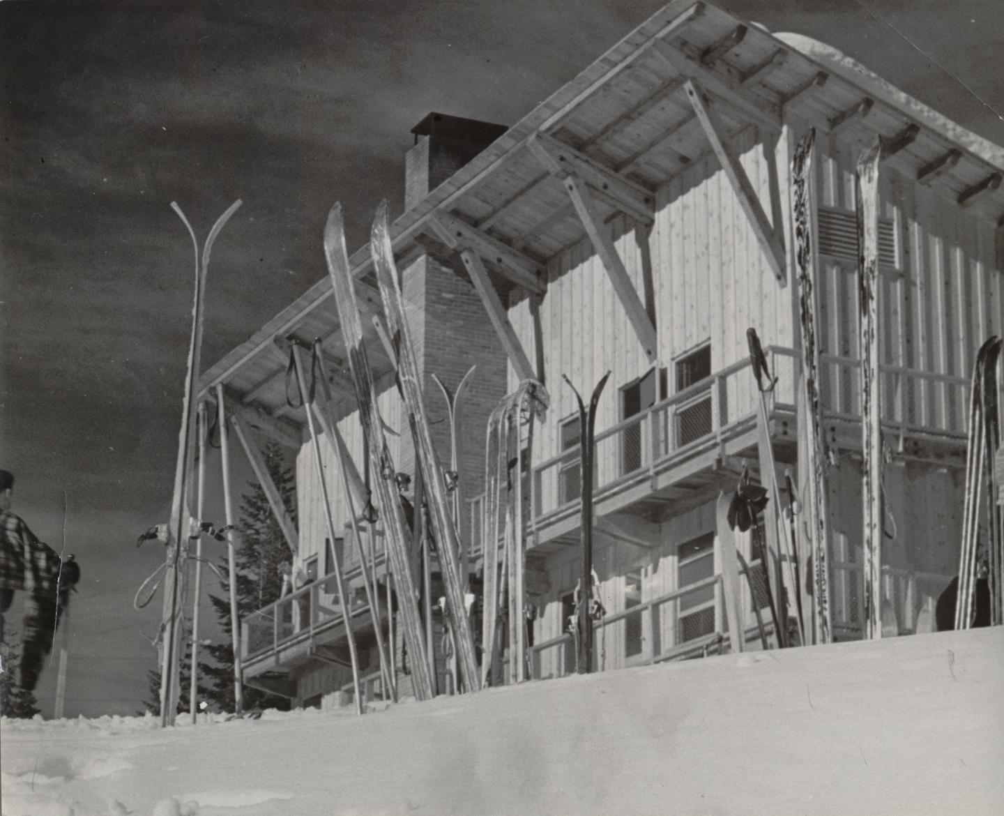 Ski lodge with skis propped against a snowy slope in black and white.