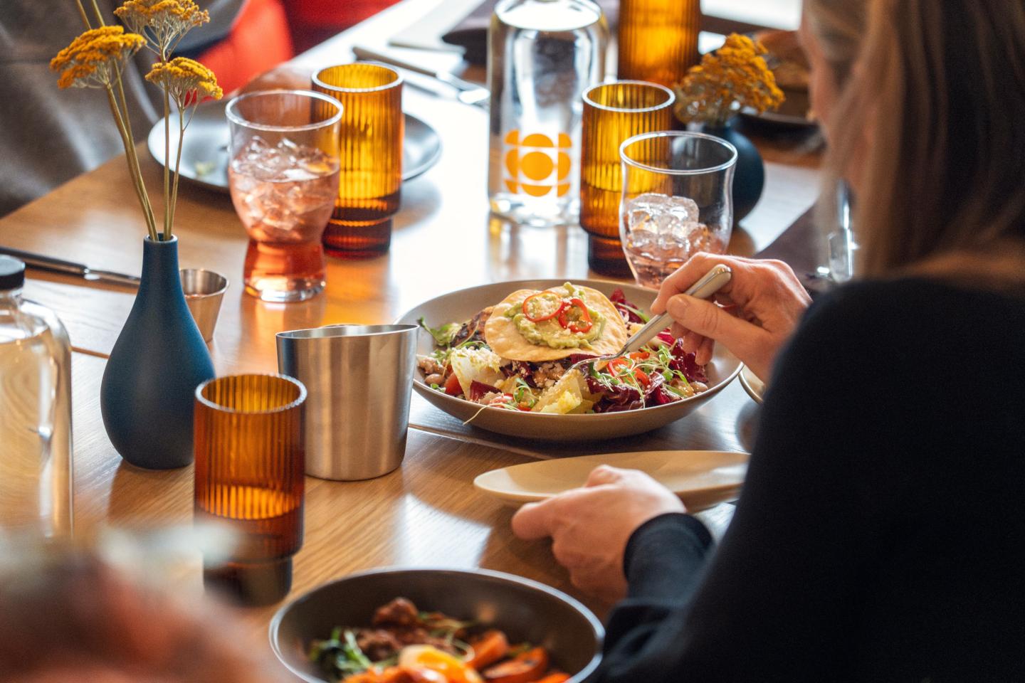 Dining table with salads, drinks, and people eating.