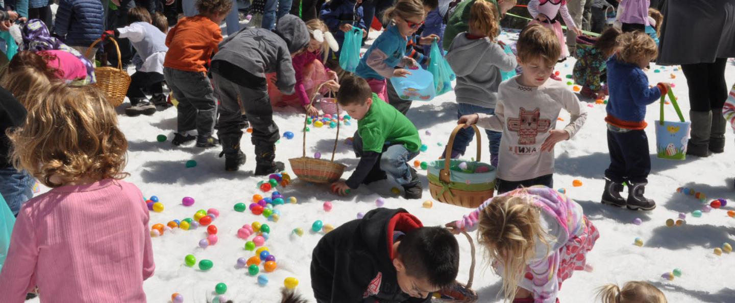 Children collecting colorful eggs on snow during an outdoor event.