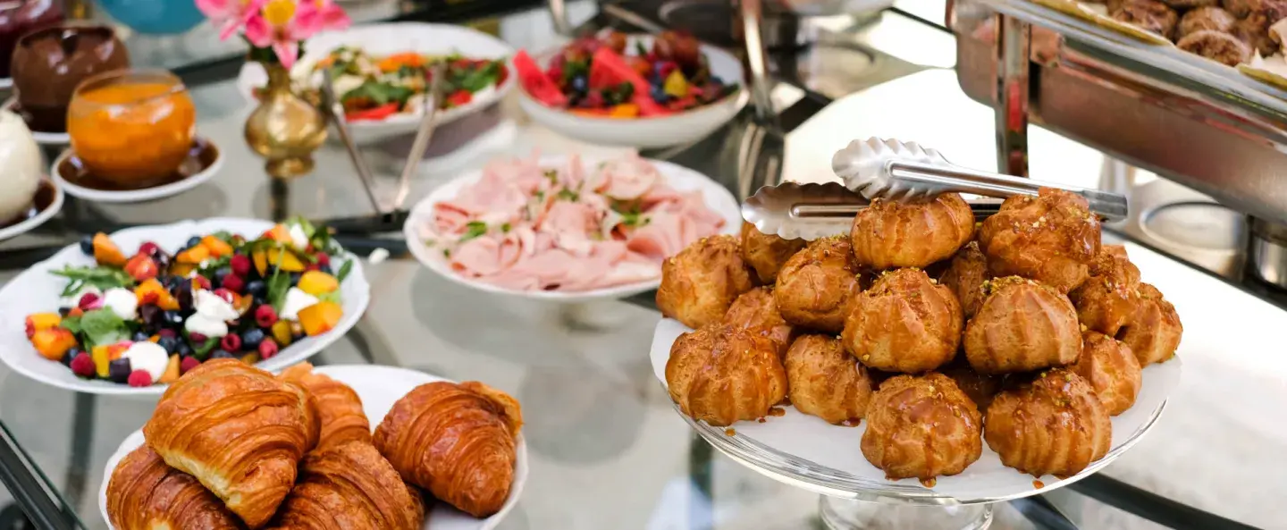 Assorted buffet with croissants and pastries on a glass table.