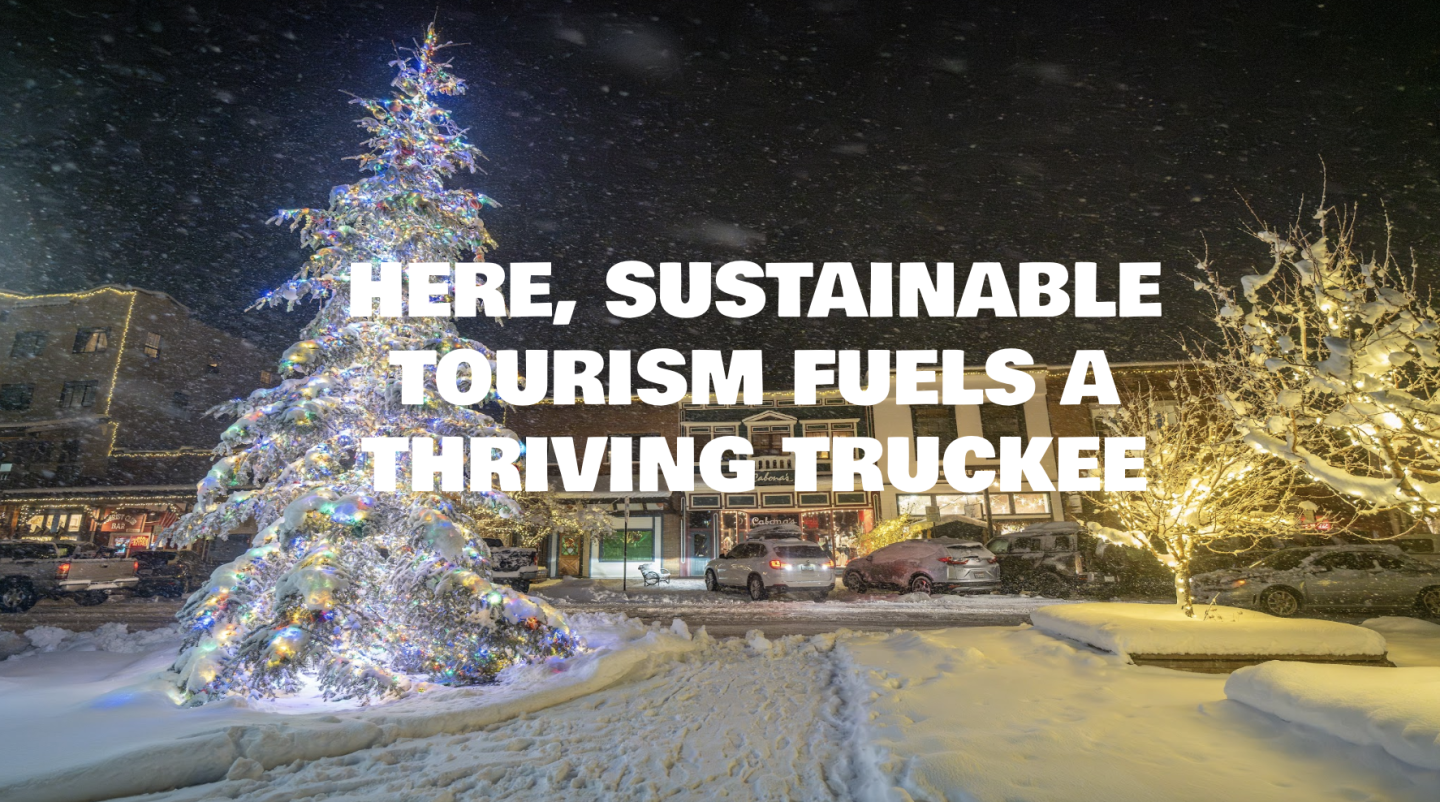 Snowy town square with lit Christmas trees at night.