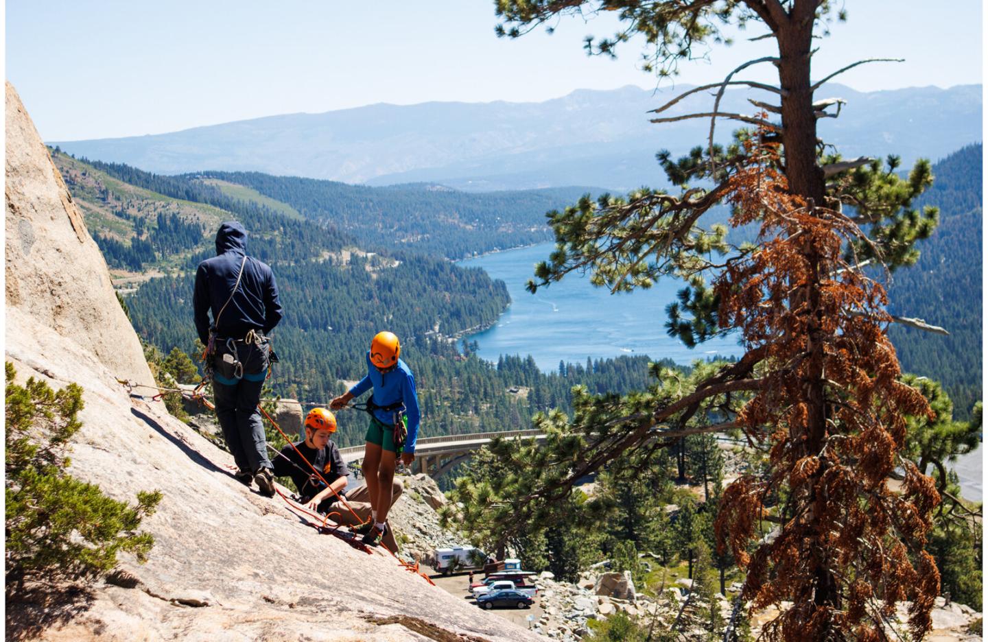 Rock climbers on a mountainside overlooking a scenic lake and forest.