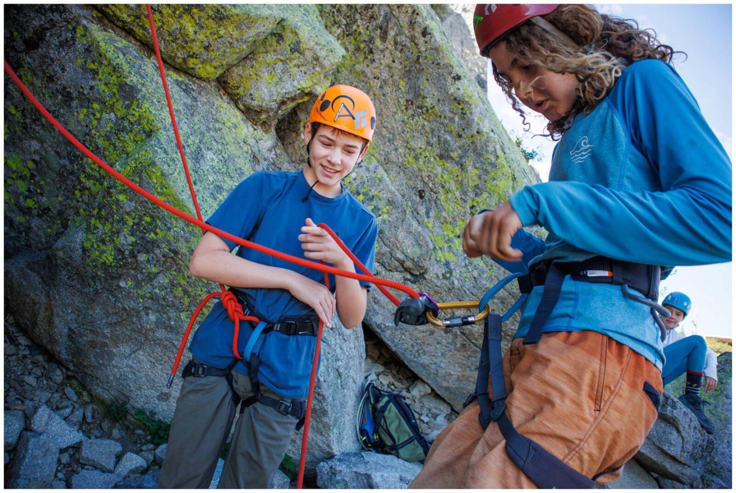 Two people in climbing gear, adjusting ropes against a rocky background.