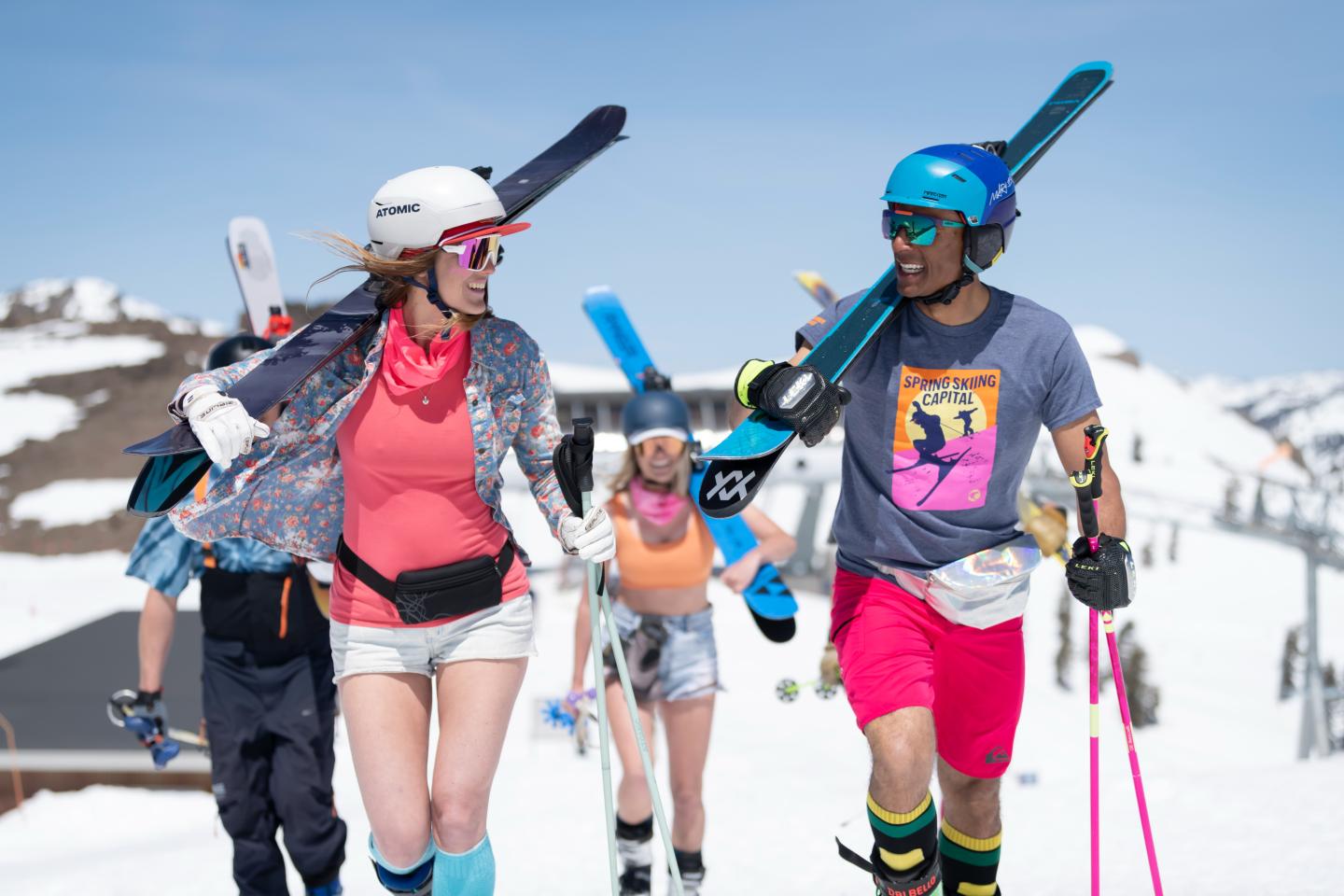Skiers in colorful outfits carrying skis, smiling on a snowy mountain.