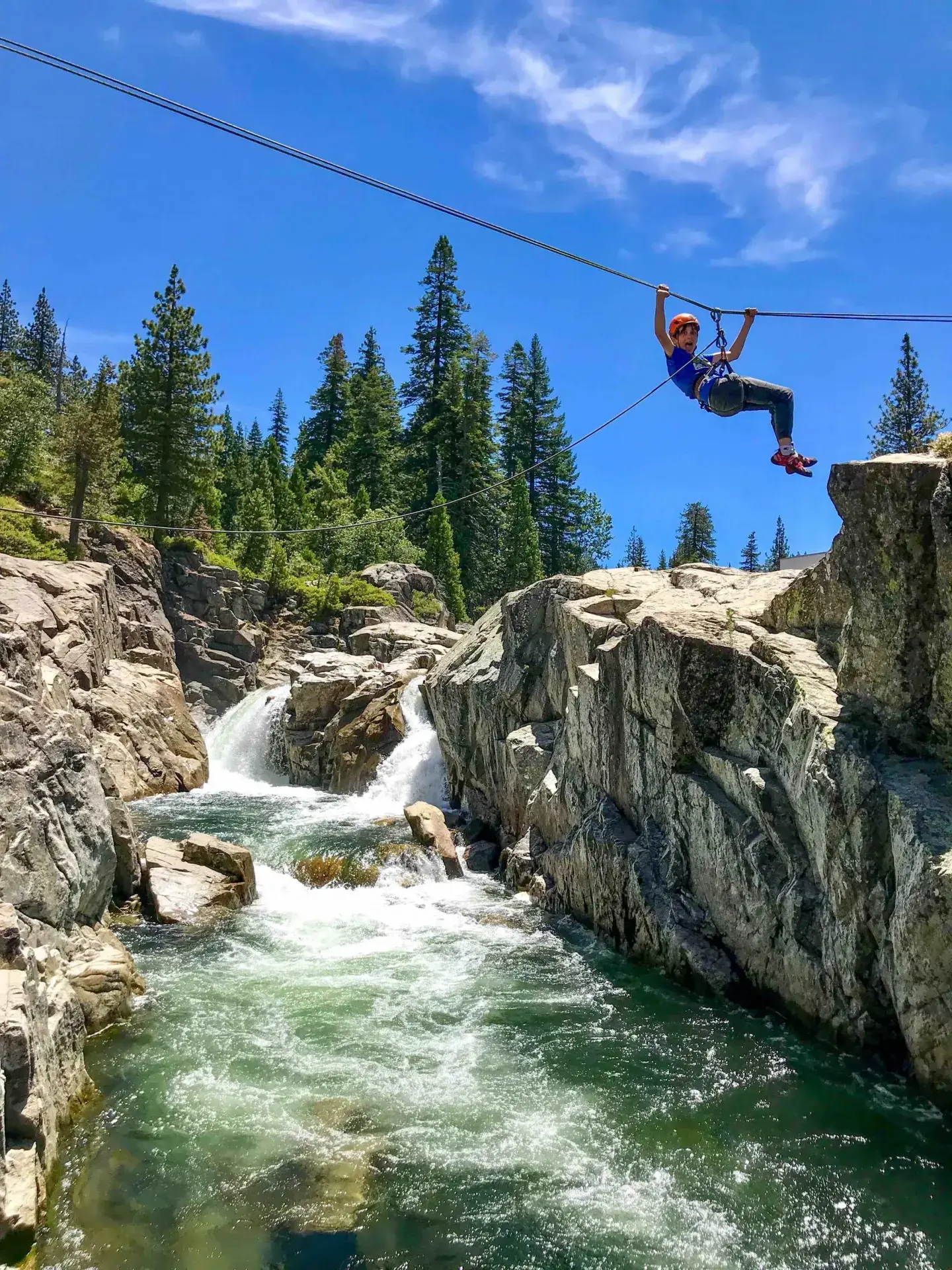 Person ziplining over river canyon, forest in the background.