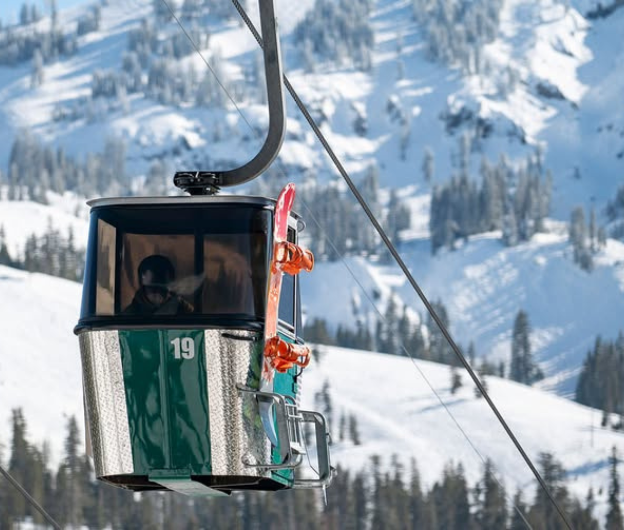 Green ski gondola with skis attached, snowy mountain backdrop.