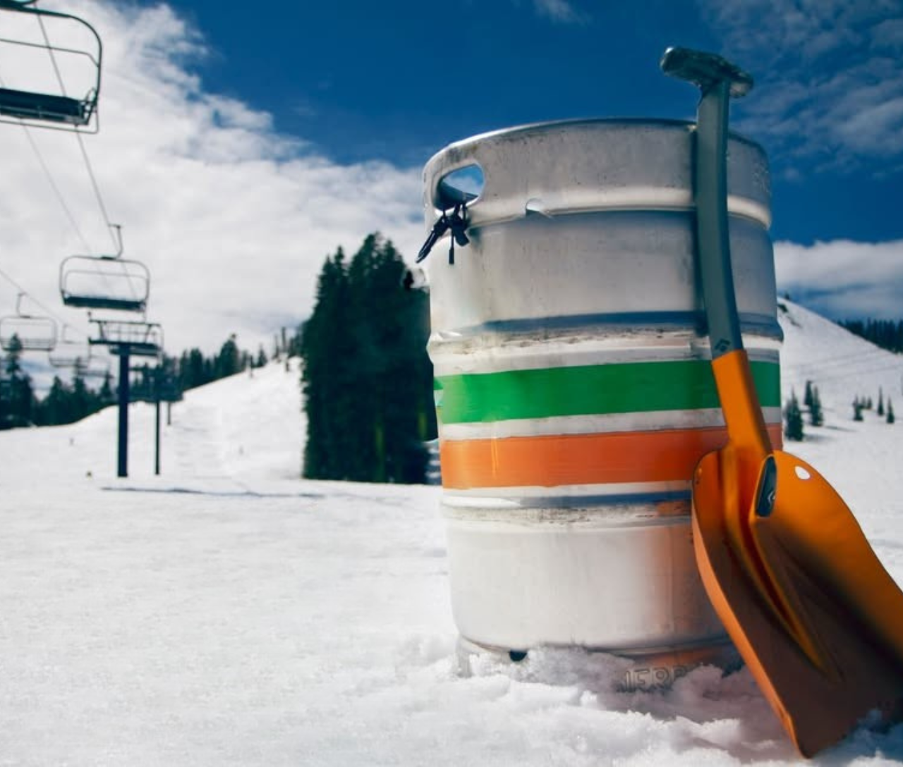 Beer keg and shovel on snowy ski slope with chairlift.