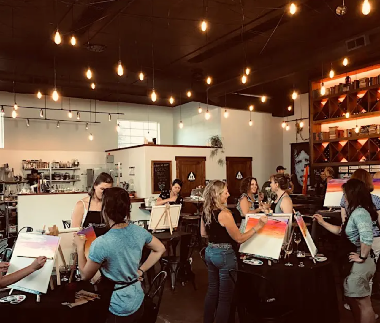 A group of people painting at easels in a warmly lit studio.