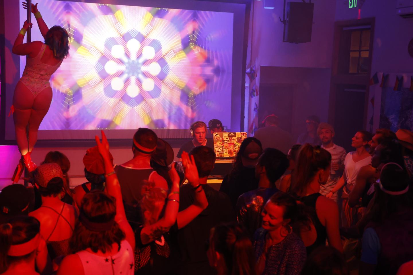 Crowded nightclub with DJ, neon lights, and a dancer on stage.