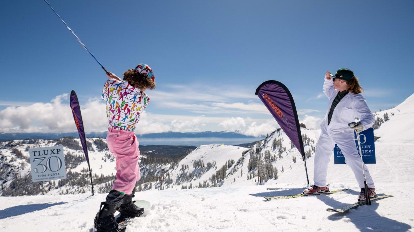 Two skiers in colorful outfits pose playfully on a snowy mountain.