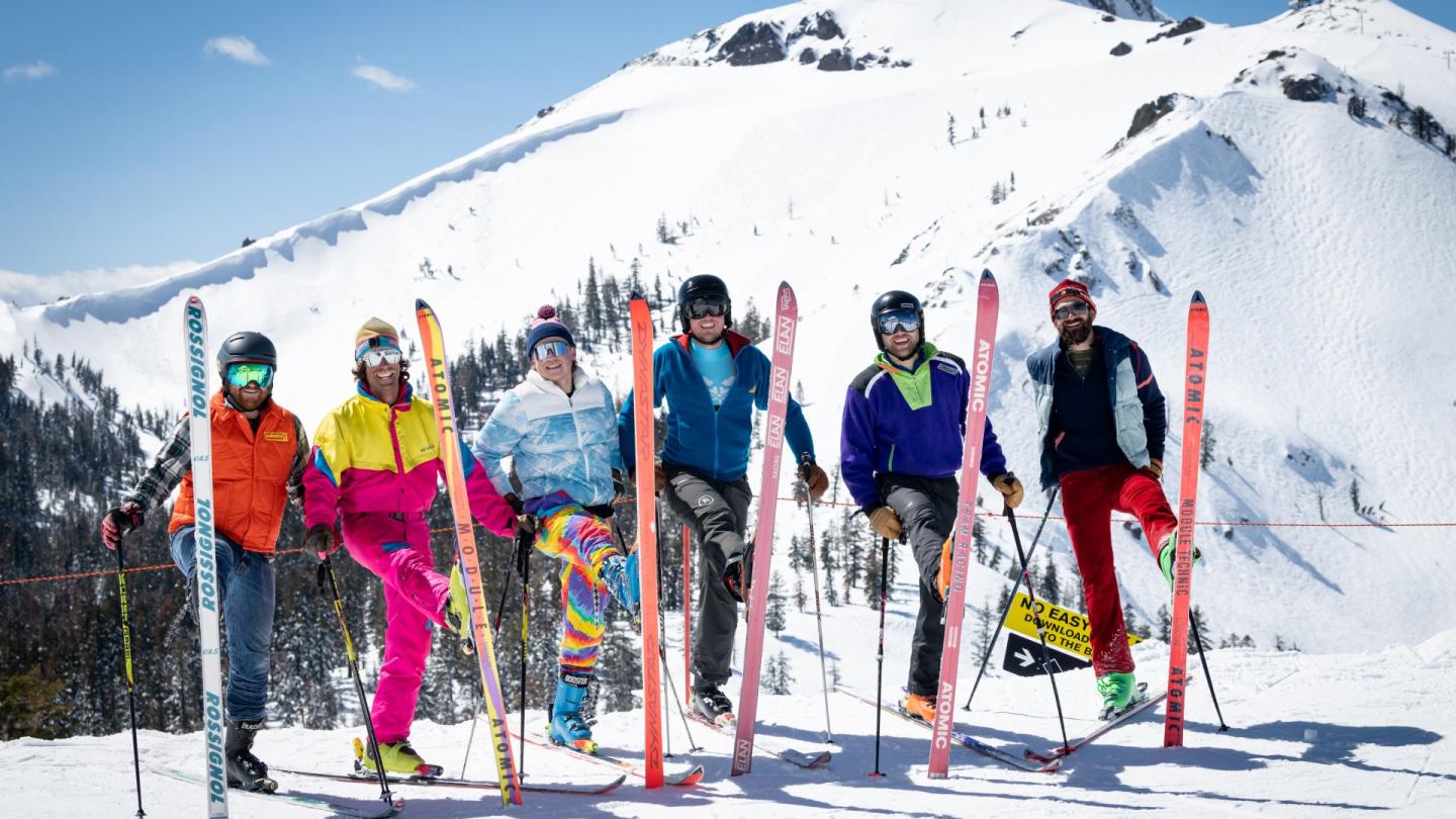 Skiers in colorful outfits on snowy mountain, clear sky above.