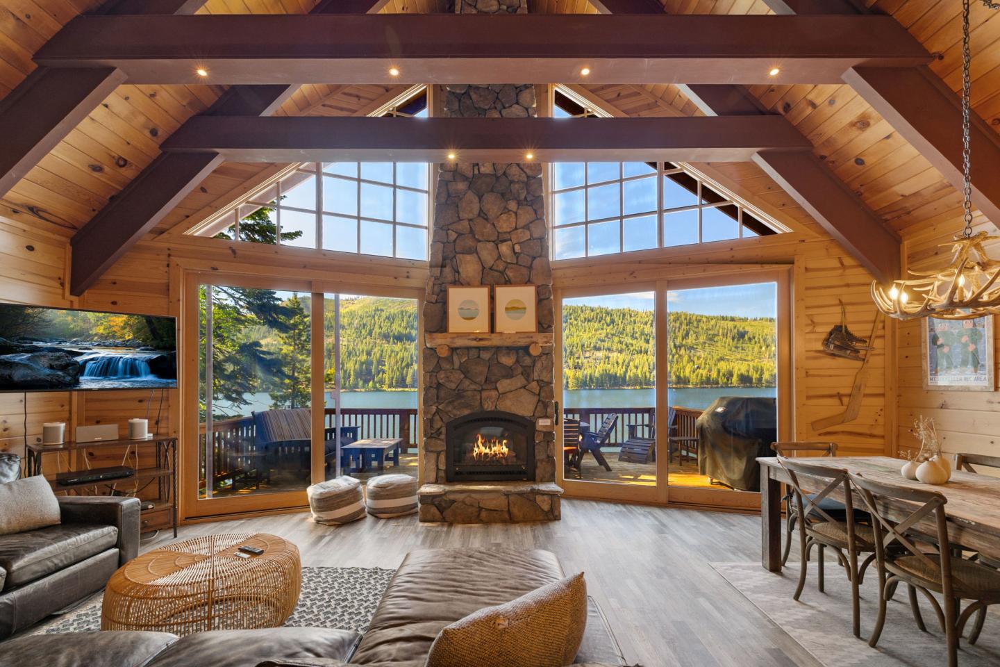 Rustic living room with a stone fireplace, lake view, and wooden beams.