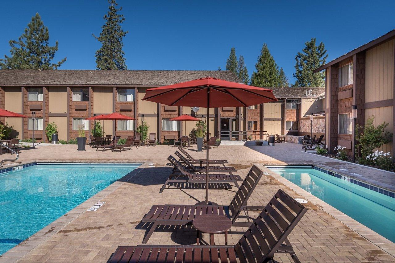 Outdoor pool with lounge chairs and red umbrellas, surrounded by buildings.