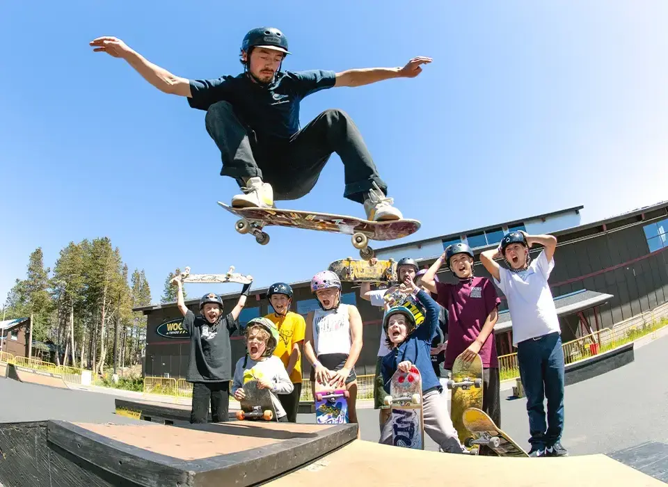 Skateboarder performs trick in front of cheering children at a skate park.