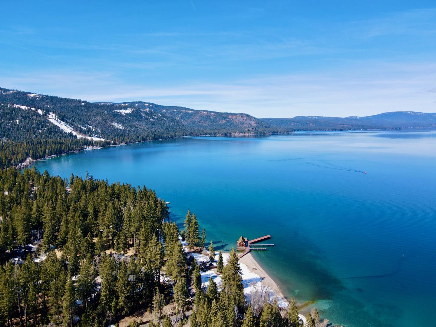 Aerial view of a clear blue lake surrounded by green pine trees and mountains.