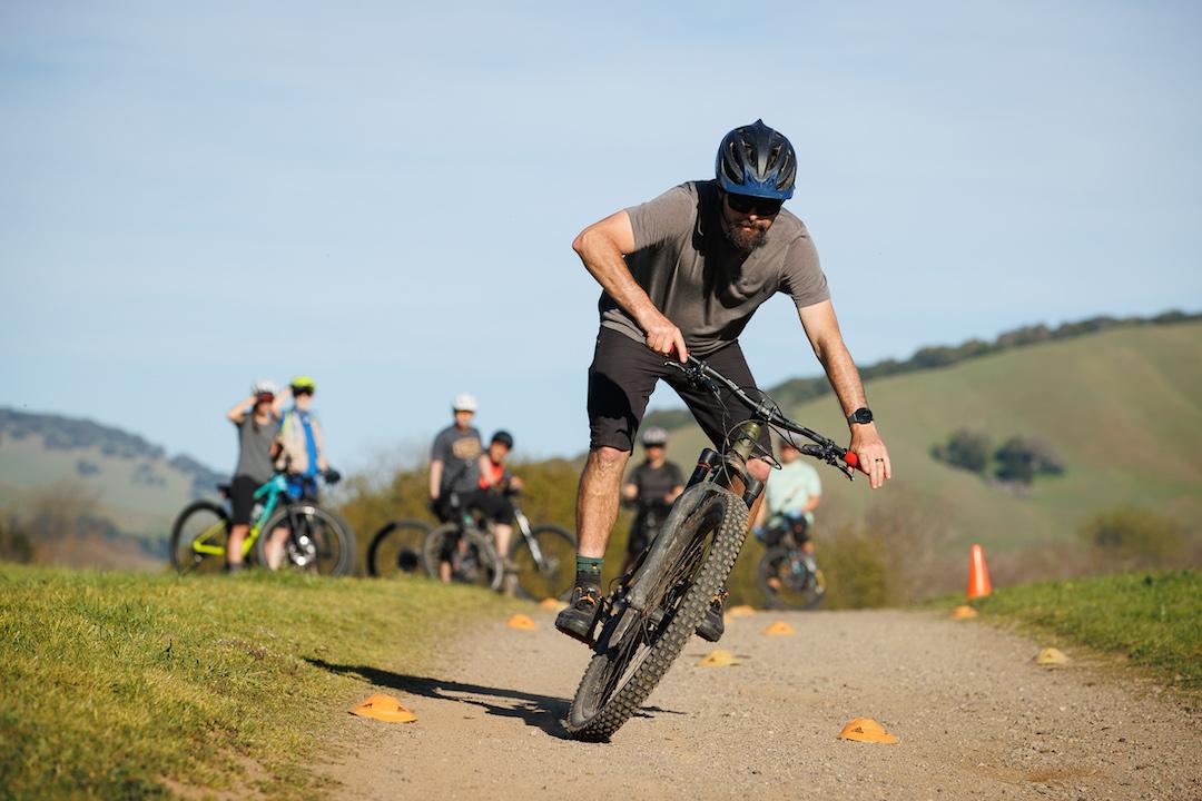Cyclist maneuvering through cones on a dirt path, with hills in the background.
