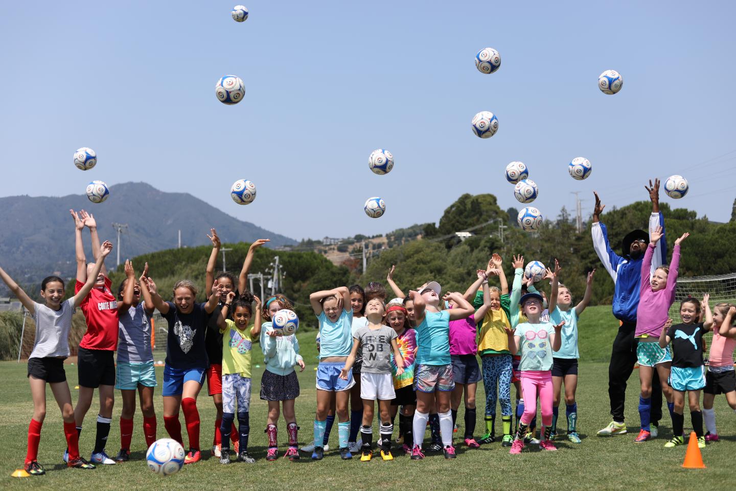 Children on a soccer field joyfully throwing balls in the air.