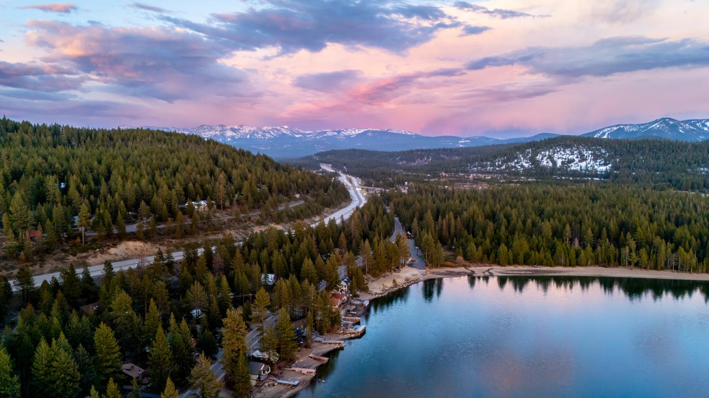 Aerial view of a lake, forest, and mountain landscape at sunset.