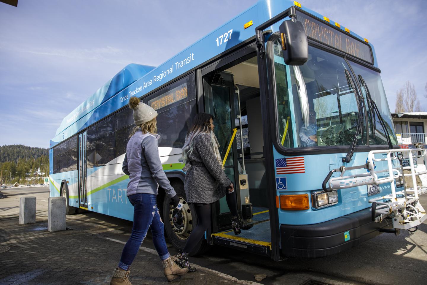 Two people board a blue bus on a clear day.