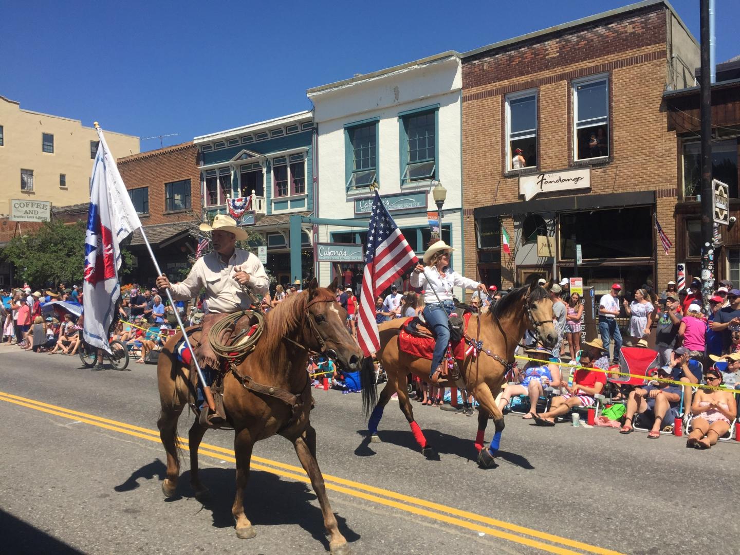 Riders on horses carrying flags in a parade on a sunny day.