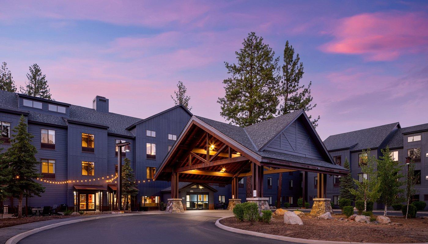 Rustic lodge entrance at sunset with warm lights and pine trees.