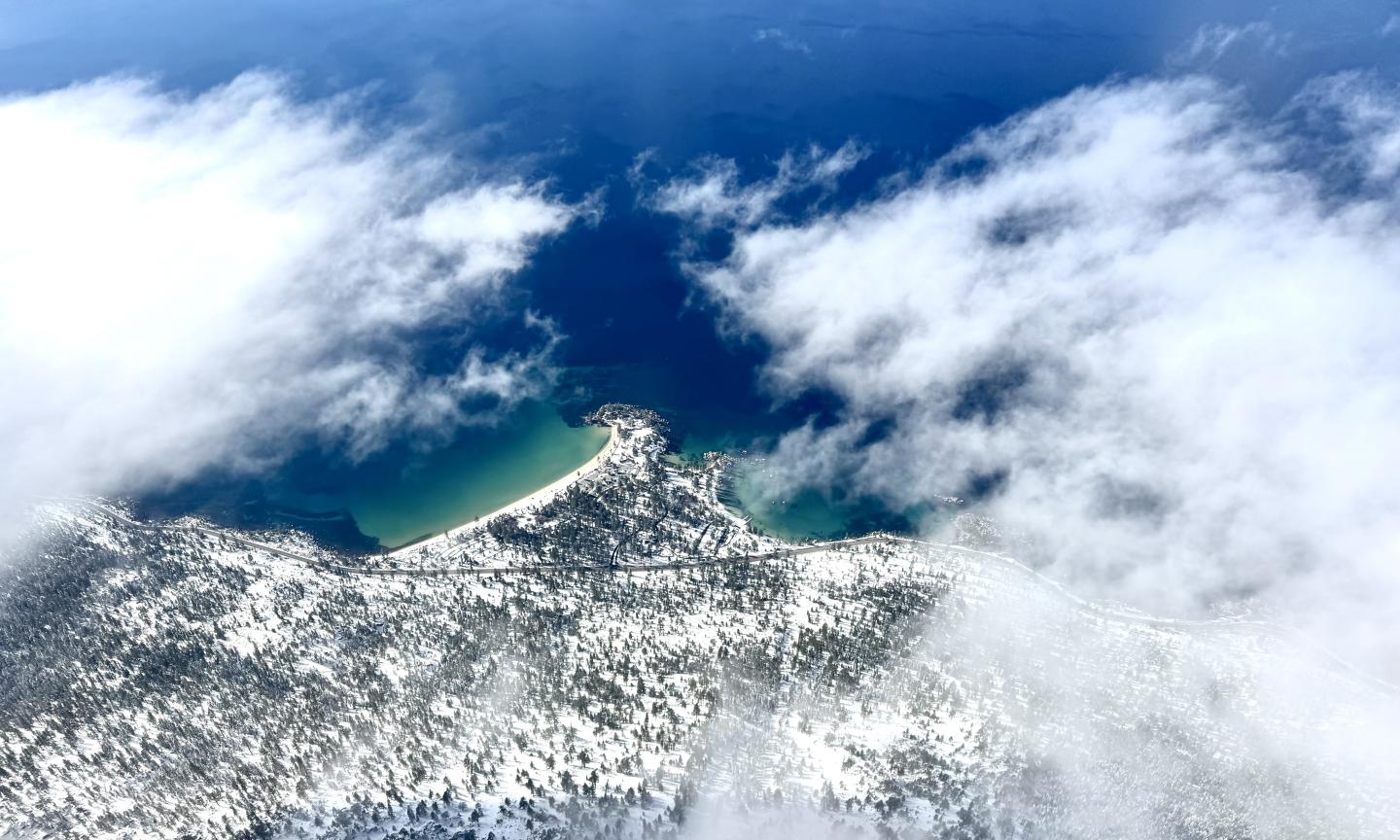 Aerial view of a snowy coastline and deep blue ocean with scattered clouds.