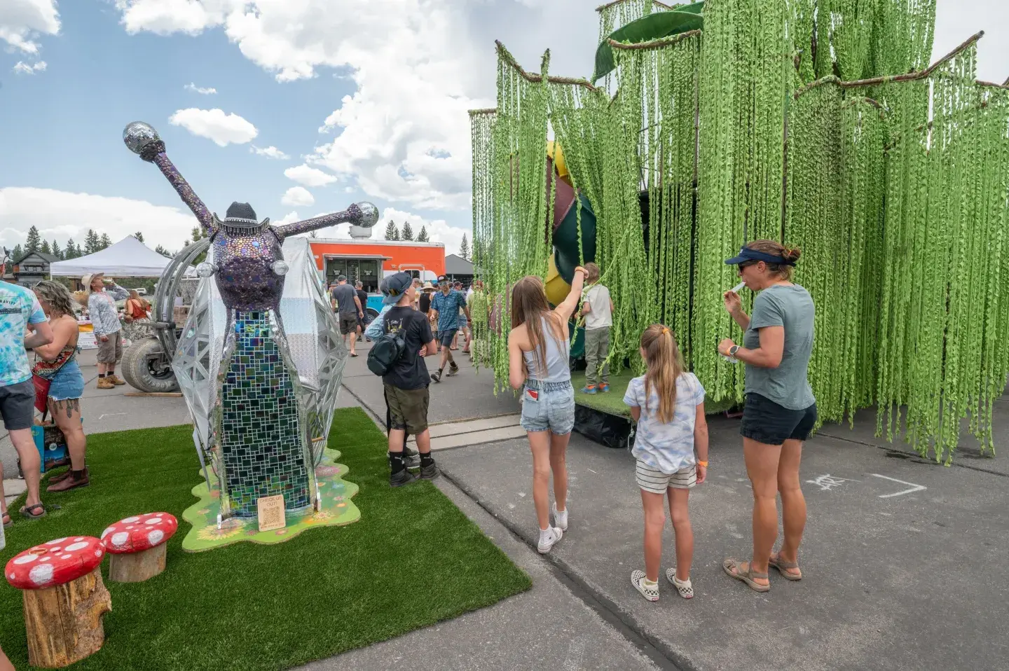 Outdoor event with people interacting with large green art installations.