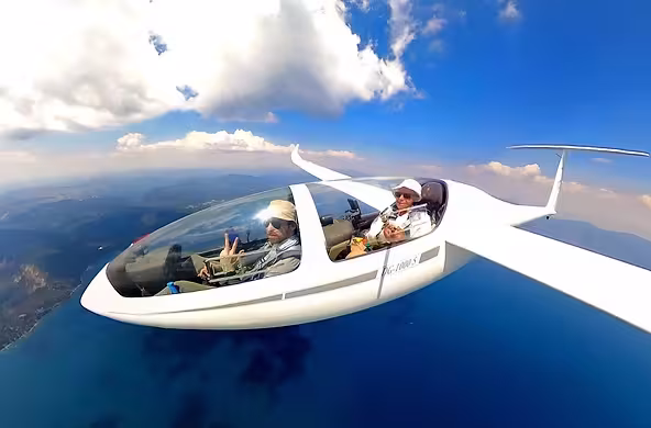 Glider flying over a scenic ocean with two passengers inside.