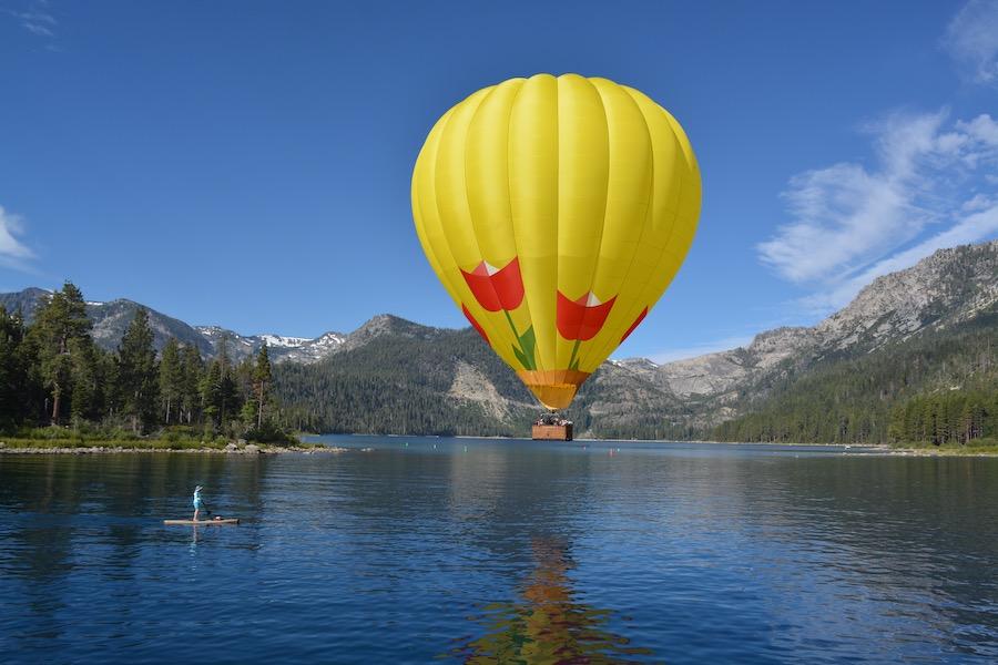 Yellow hot air balloon over a lake with mountains in the background.