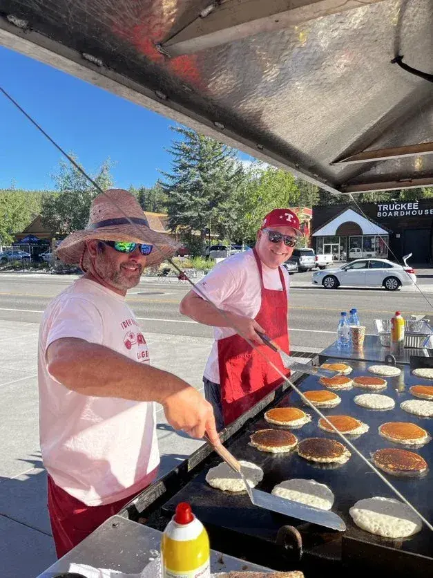 Two people cooking pancakes outdoors on a large griddle.