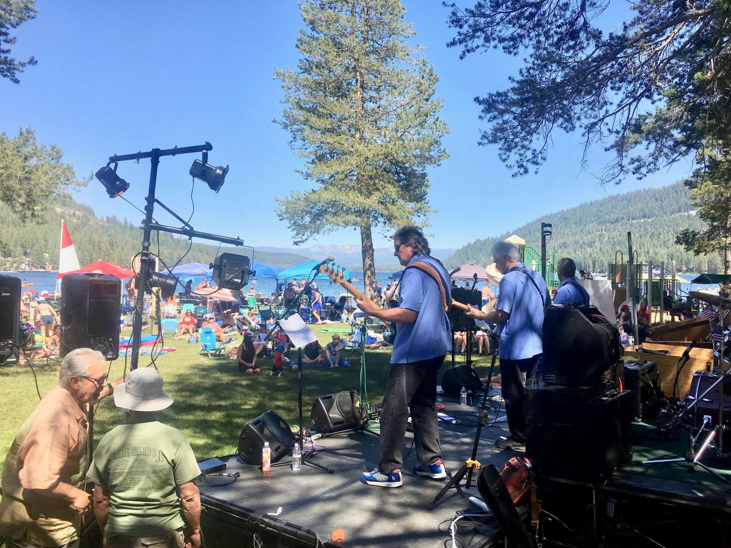 Band performing outdoors at a park, with a crowd and trees.