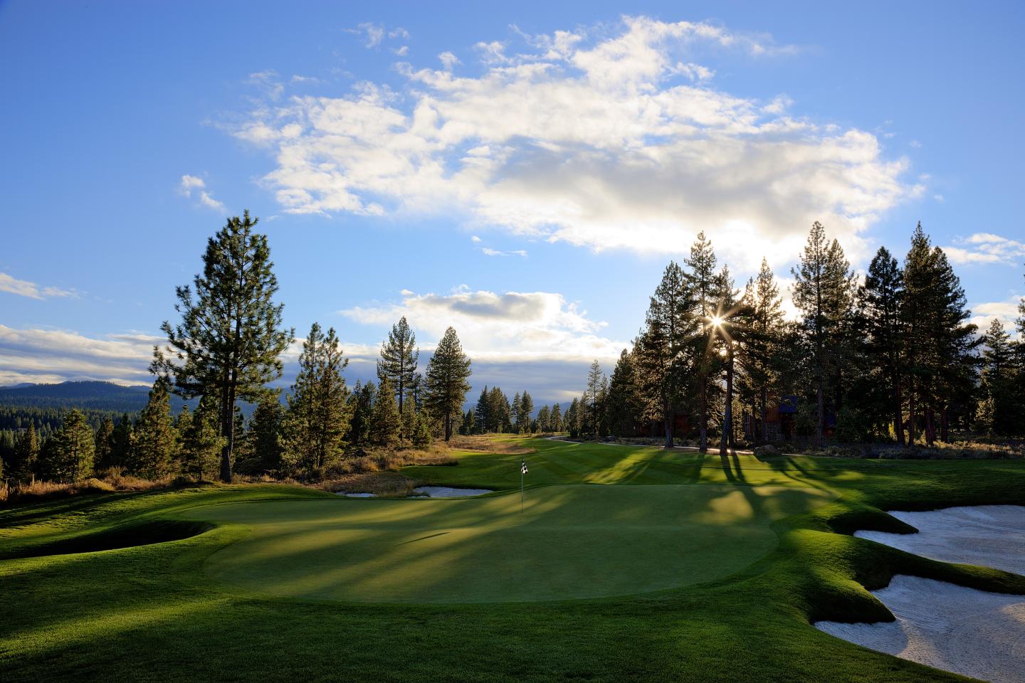Sunny golf course with trees, blue sky, and clouds.
