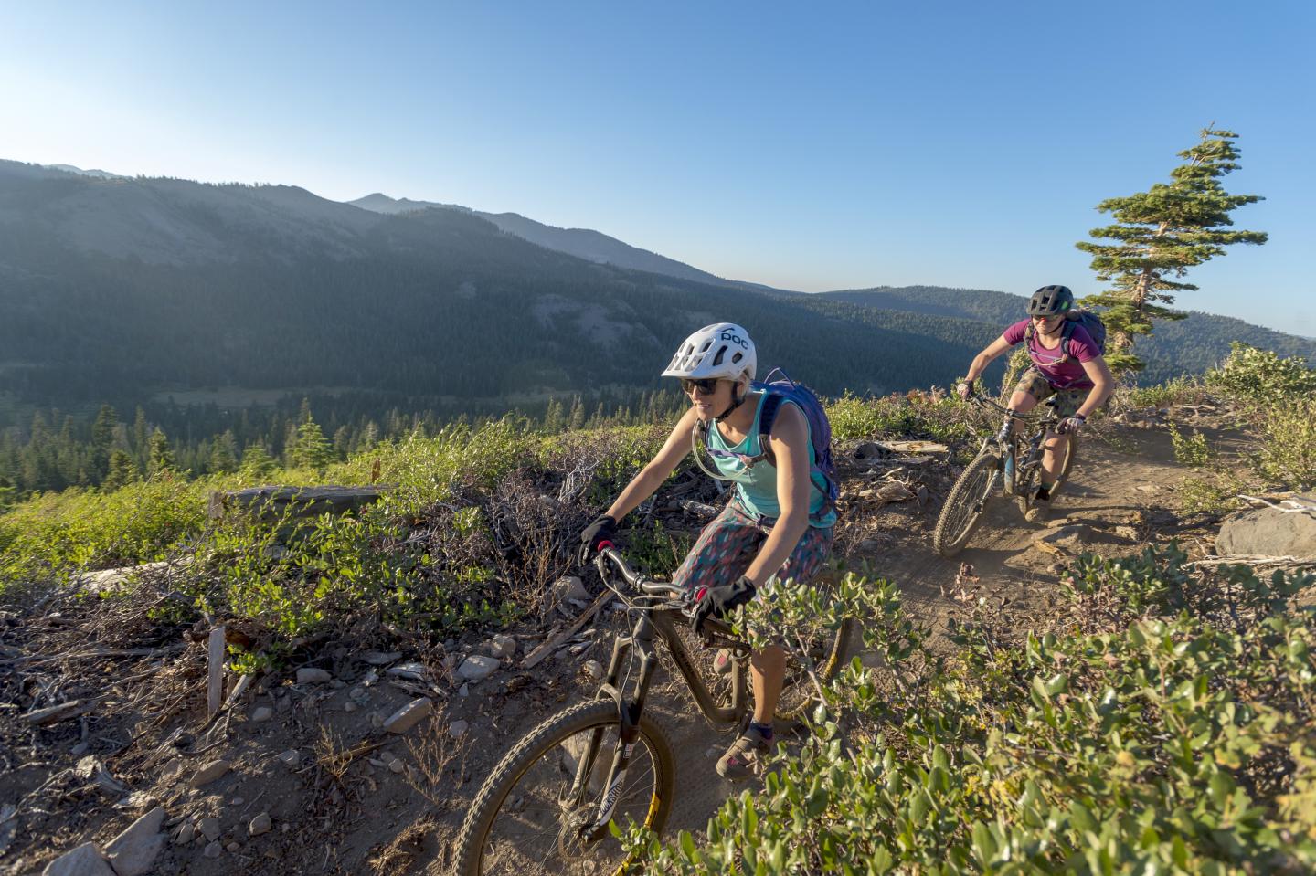 Two cyclists on a mountain trail with a scenic landscape.