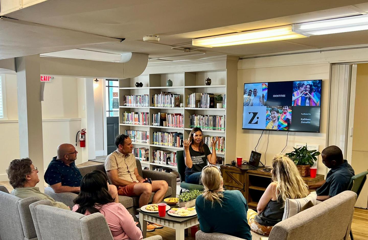 A group of people in a cozy room having a discussion with presentations on a screen.