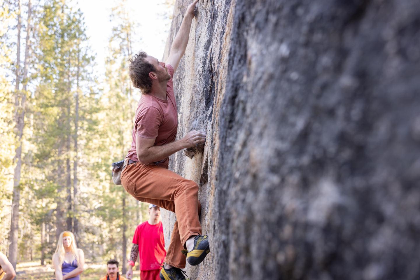 Climber scaling a rocky surface, trees in the background.