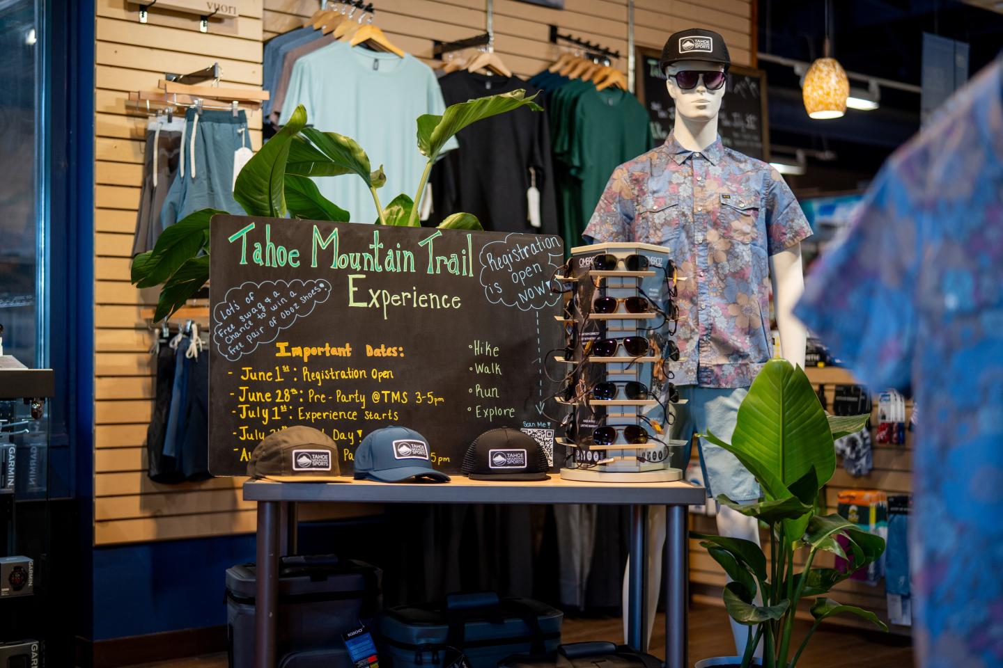 Mannequin in floral shirt, store display with hats and sunglasses stand, plant décor.