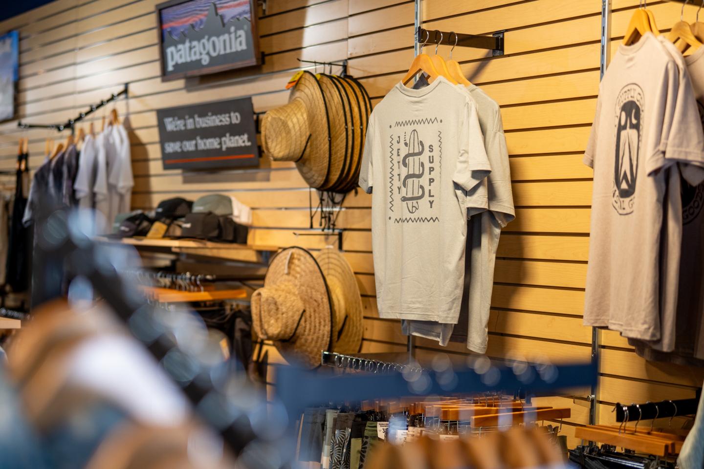 Clothing store display with hats and T-shirts on a wooden wall.