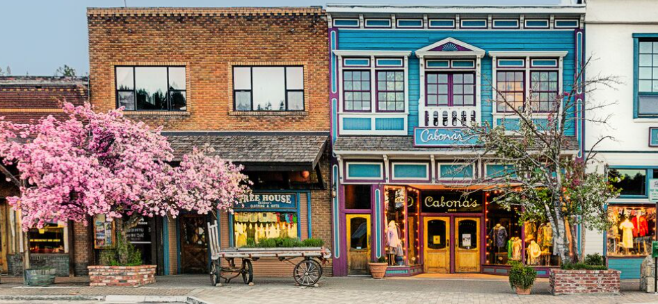 Colorful storefronts with blooming trees on a quaint street.
