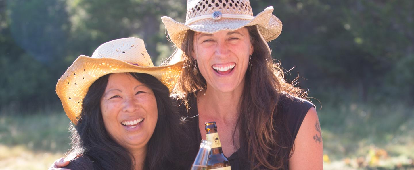 Two women in cowboy hats smiling in a sunny outdoor setting.
