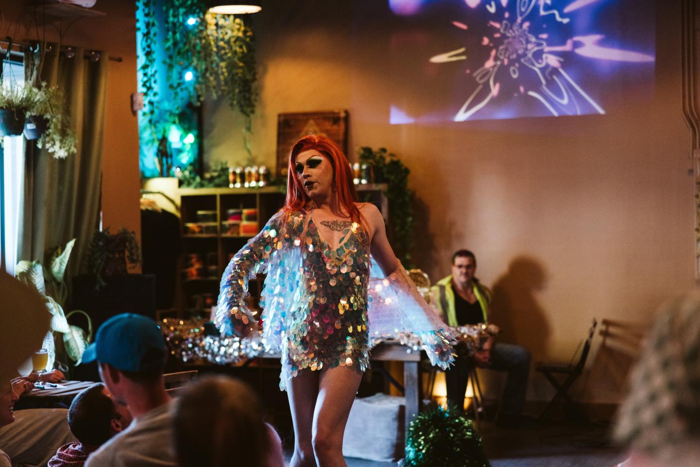 Performer in sequin dress on stage with colorful lights.