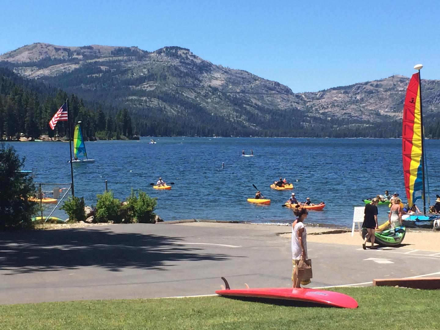 Lake scene with kayakers, mountains, and colorful surfboards on the shore.