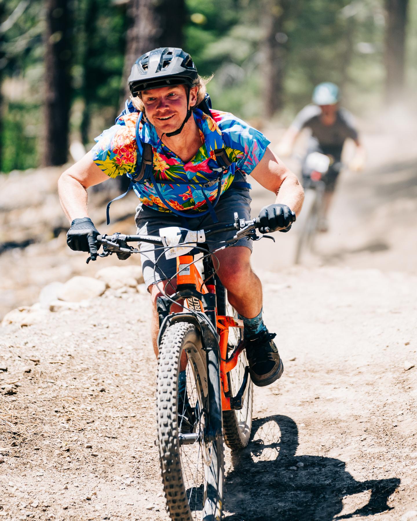 Cyclist in colorful shirt rides uphill on a mountain trail.