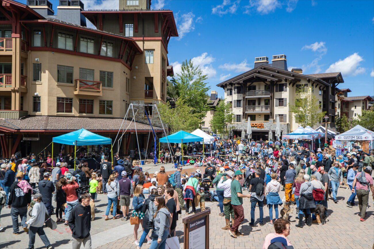 Crowd enjoying a sunny outdoor festival by buildings with blue tents.