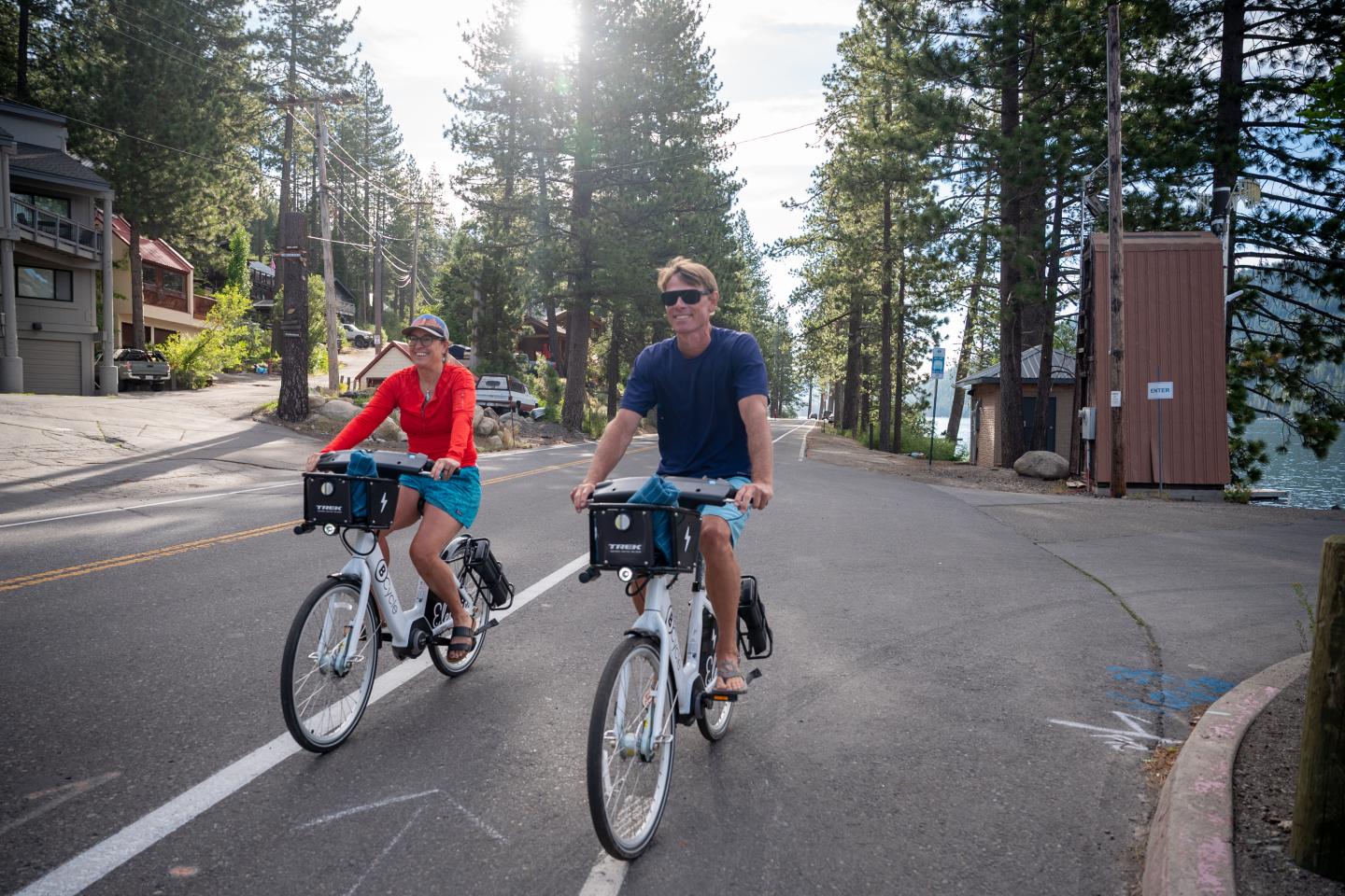 Two people cycling down a sunny, tree-lined street.