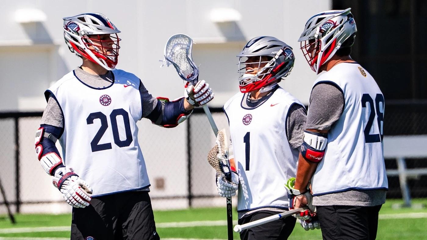 Three lacrosse players in gear talking on the field.