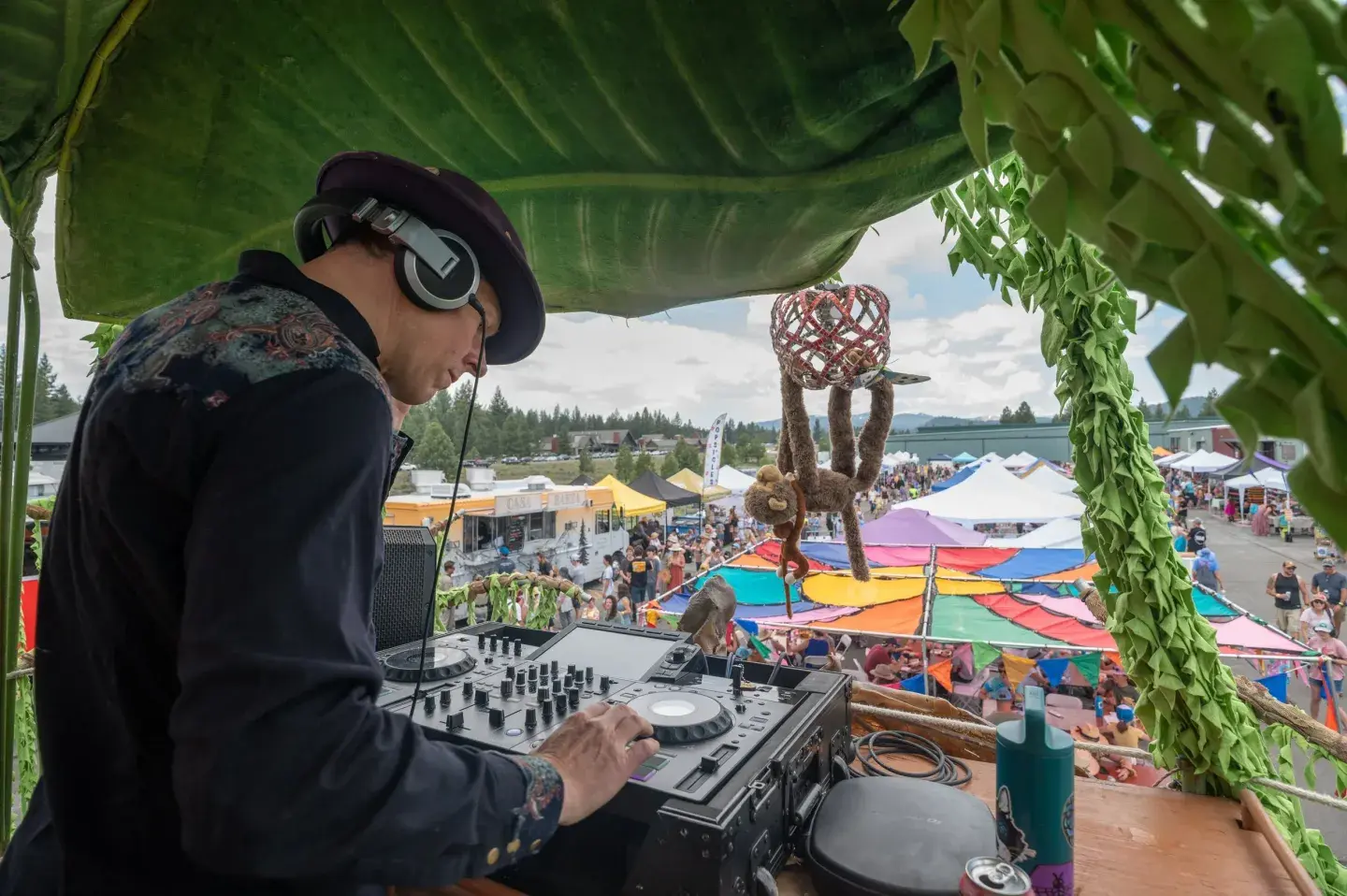 DJ performing outdoors under leafy canopy at a colorful festival.