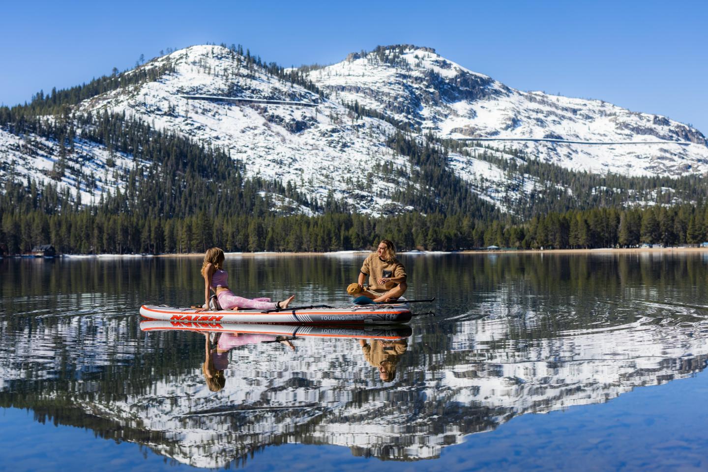 Two people canoeing on a calm lake, snowy mountains behind.